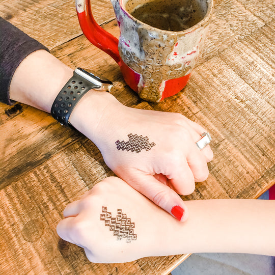 mother and daughter with matching scripture memory temporary tattoos. Wooden table with red clay mug.